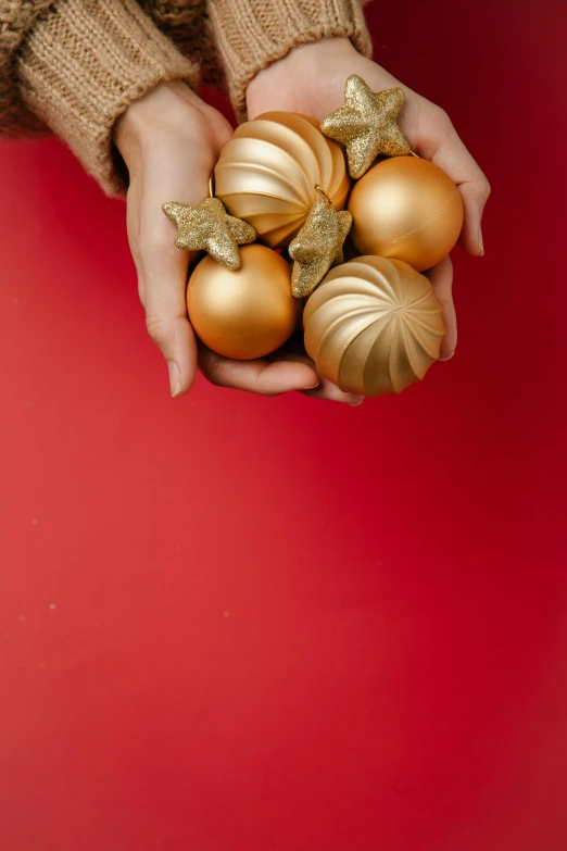 a person holding gold ornaments in their hands, on a red background, holiday vibe, how-to, on grey background