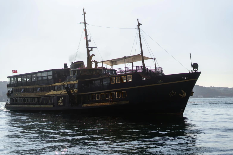 a large boat floating on top of a body of water, inspired by Ismail Inceoglu, unsplash, hurufiyya, gold and black color scheme, istanbul, arma 3 screenshot, front side