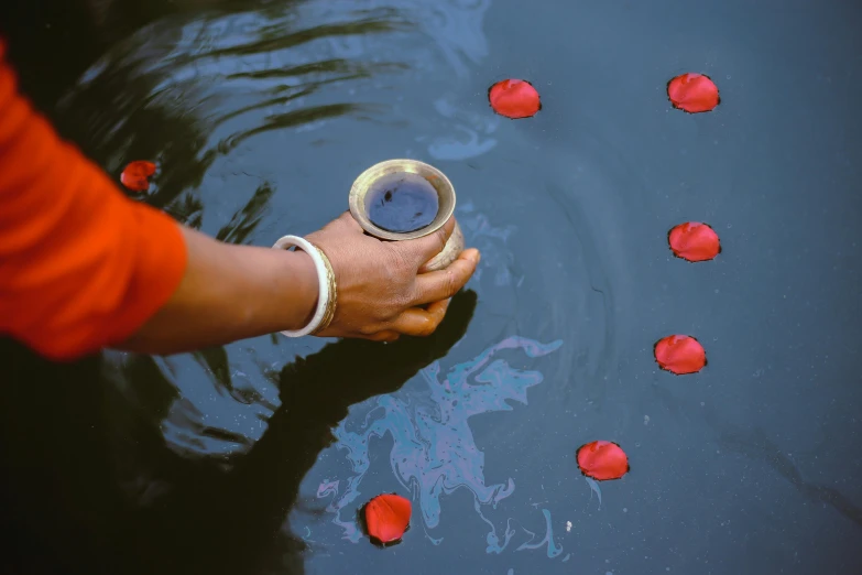 a person holding a cup in a body of water, an album cover, inspired by Steve McCurry, pexels contest winner, hurufiyya, kalighat flowers, indigo and venetian red, rituals, 15081959 21121991 01012000 4k