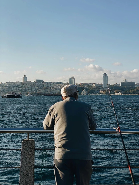 a man standing on top of a pier next to a body of water, istanbul, fishing pole, 2022 photograph, facing away