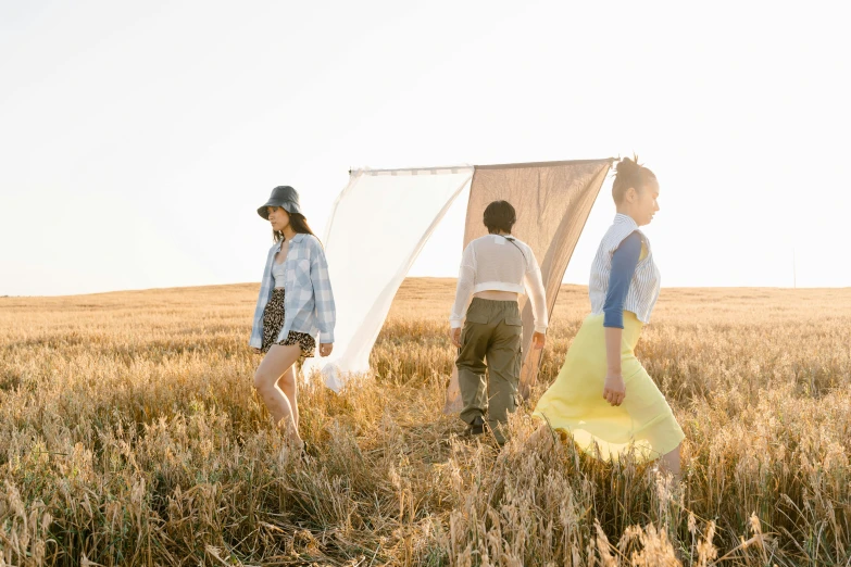 a group of people standing in a field, an album cover, by Jessie Algie, unsplash, conceptual art, clothes floating, three views, picnic, uniform off - white sky