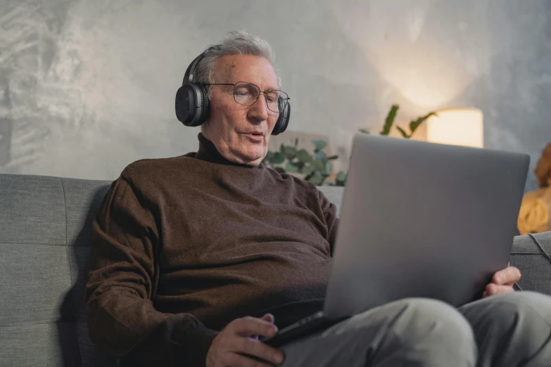 a man sitting on a couch with a laptop and headphones, trending on pexels, an oldman, avatar image, warwick saint, wearing a headset