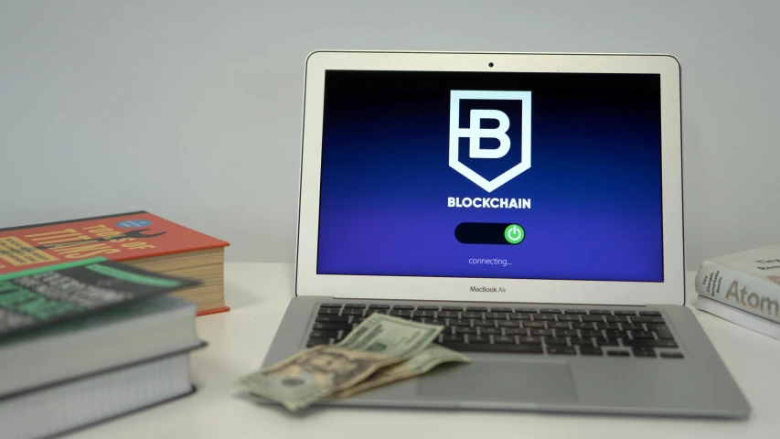 a laptop computer sitting on top of a desk next to a stack of books, a digital rendering, unsplash, blockchain vault, zoomed view of a banknote, splashscreen, chain