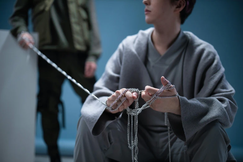 a man sitting on the ground with a chain around his neck, inspired by Itō Ogura Yonesuke, unsplash, hyperrealism, film still from harry potter, with prison clothing, cai xukun, movie scene close up