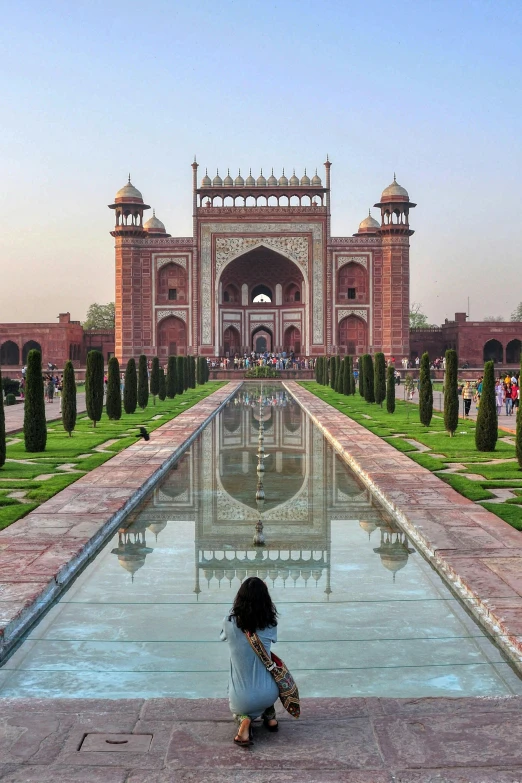 a woman sitting on the edge of a pool in front of a building, inspired by Steve McCurry, arabesque, huge gate, taj mahal, panoramic centered view of girl, parks and gardens