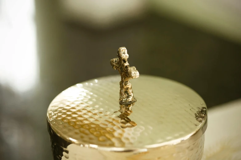 a close up of a metal object on a table, inspired by Diego Giacometti, happening, jar of honey, jesus on cross, top lid, gold plated