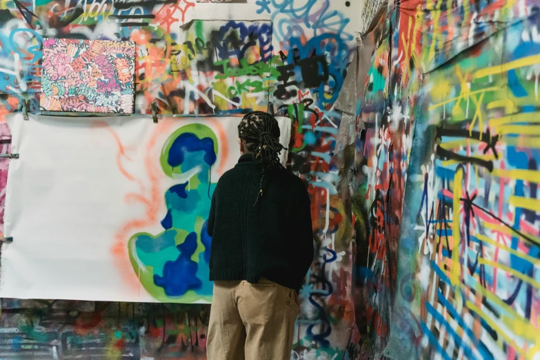 a man standing in front of a wall covered in graffiti, trending on unsplash, graffiti, stands at a his easel, multi colored, over the shoulder view, mid shot photo