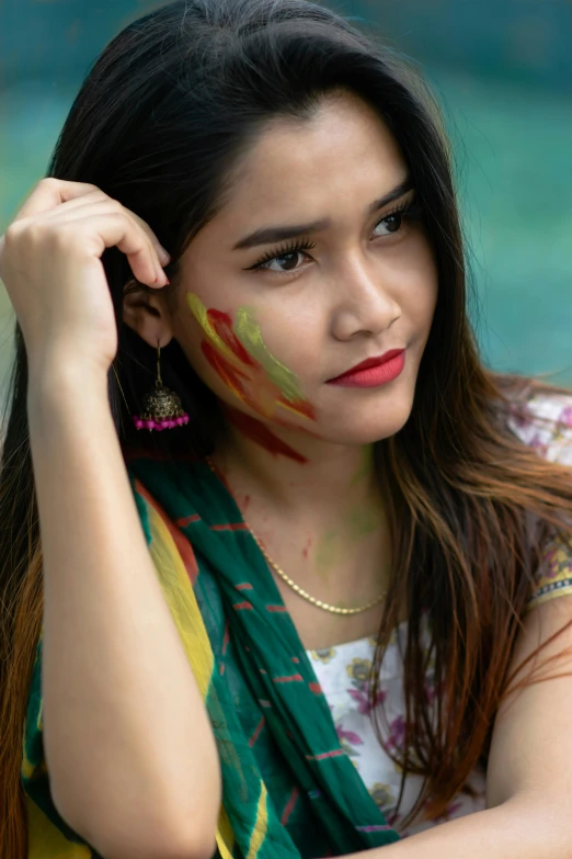 a woman that is sitting down with some paint on her face, a picture, trending on pexels, assamese, green magenta and gold, handsome girl, wearing jewelry