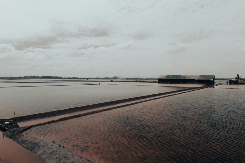 a large body of water sitting under a cloudy sky, inspired by Andreas Gursky, unsplash contest winner, minimalism, red dusty soil, buildings covered in black tar, paddy fields and river flowing, trending on vsco