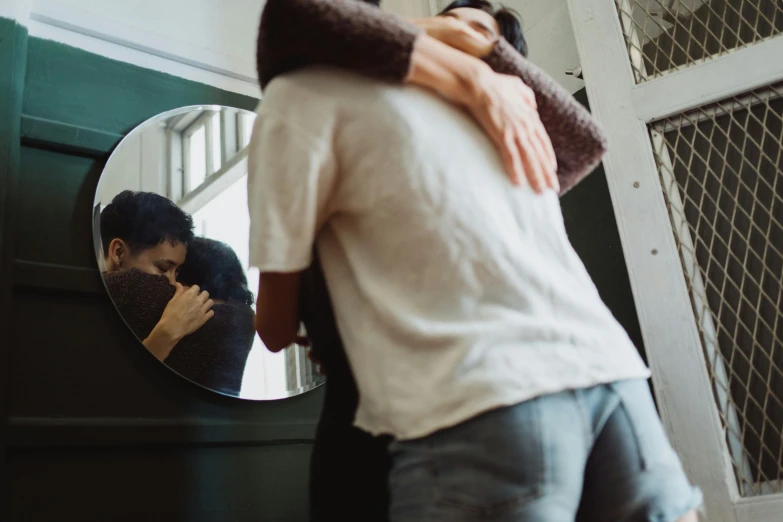 a man hugging a woman in front of a mirror, pexels contest winner, happening, leaving a room, lesbian embrace, looking through a portal, ad image