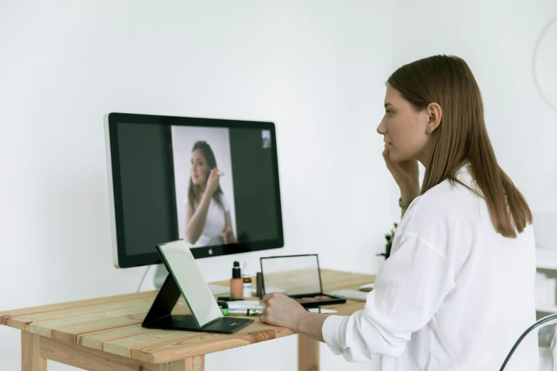 a woman sitting at a desk in front of a computer, trending on pexels, video art, doctors mirror, two models in the frame, brown, easel