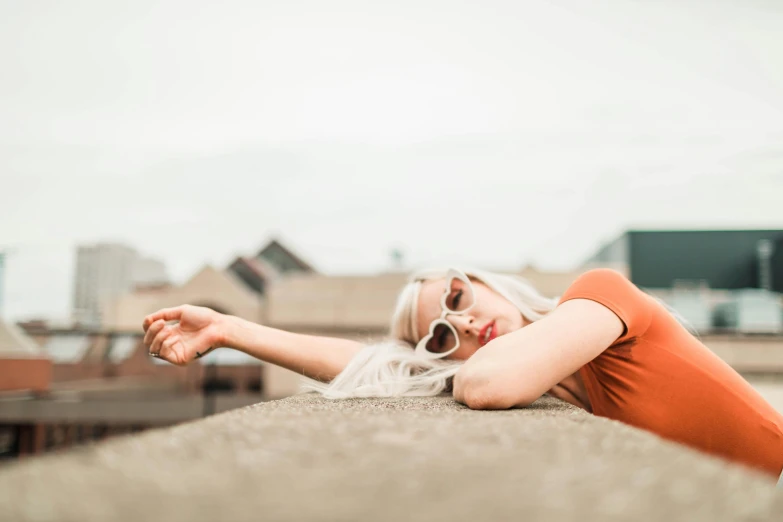 a woman laying on top of a cement wall, by Lee Loughridge, trending on pexels, orange sunglasses, perfect white haired girl, rooftop party, hand on her chin