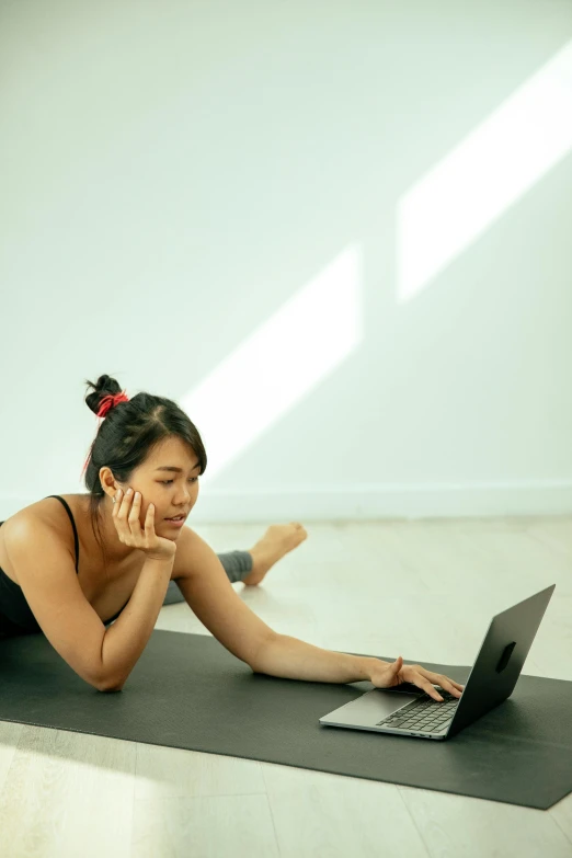 a woman laying on a yoga mat using a laptop, a picture, happening, digital still, li zixin, concerned expression, profile image