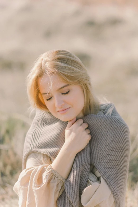 a woman wrapped in a blanket in a field, trending on unsplash, romanticism, anna nikonova aka newmilky, young blonde woman, soft shadows, wearing a sweater