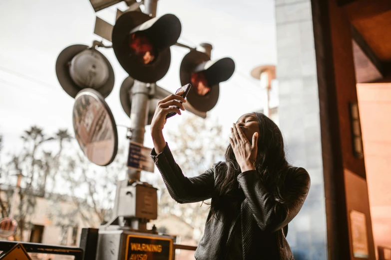 a woman taking a picture of a train crossing signal, by Dan Frazier, pexels contest winner, interactive art, standing in a restaurant, showing her face, holding it out to the camera, good light