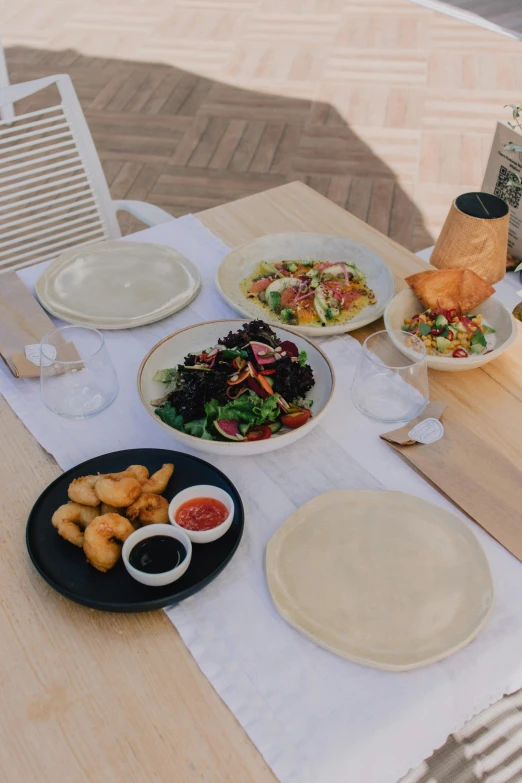 a table topped with plates of food on top of a wooden table, by Nicolette Macnamara, seaside, salad, order, dumplings on a plate