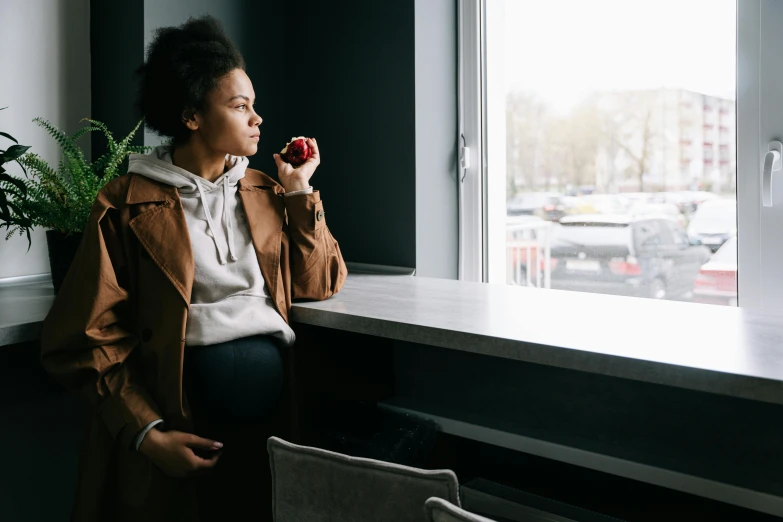 a woman sitting on a window sill talking on a cell phone, by Emma Andijewska, trending on pexels, realism, holding an apple, black young woman, standing in a restaurant, pregnancy