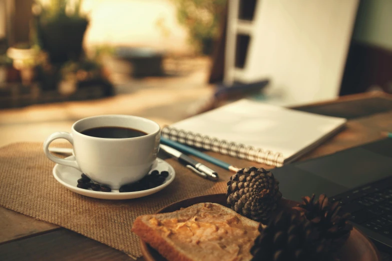 a cup of coffee and a piece of bread on a table, pexels contest winner, writing on a clipboard, black and brown colors, nature outside, thumbnail