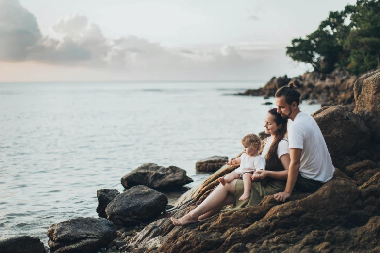 a man and woman sitting on a rock next to the ocean, by Adam Marczyński, pexels contest winner, portrait of family of three, avatar image, high quality upload, ad image