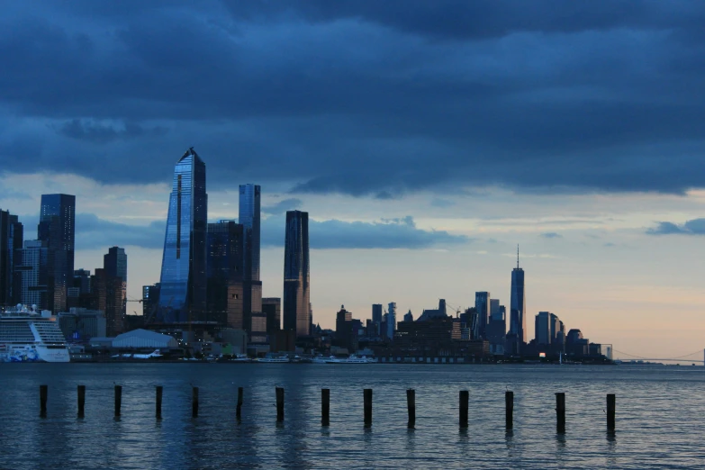 a large body of water with a city in the background, by Jessie Algie, unsplash contest winner, modernism, new york skyline, humid evening, tall metal towers, late afternoon light