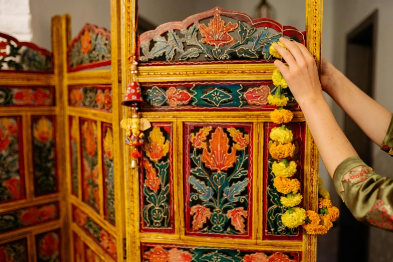 a close up of a person holding a piece of art, by Julia Pishtar, trending on unsplash, arts and crafts movement, indian temple, lots of decoration and furniture, yellow and red color scheme, decorated with flowers