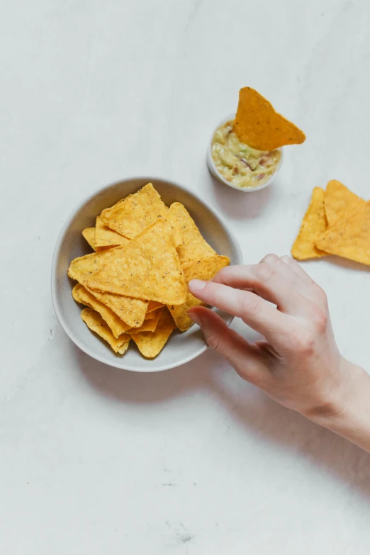 a person reaching for a bowl of tortilla chips, by Jessie Algie, square, plating, lumen, grey