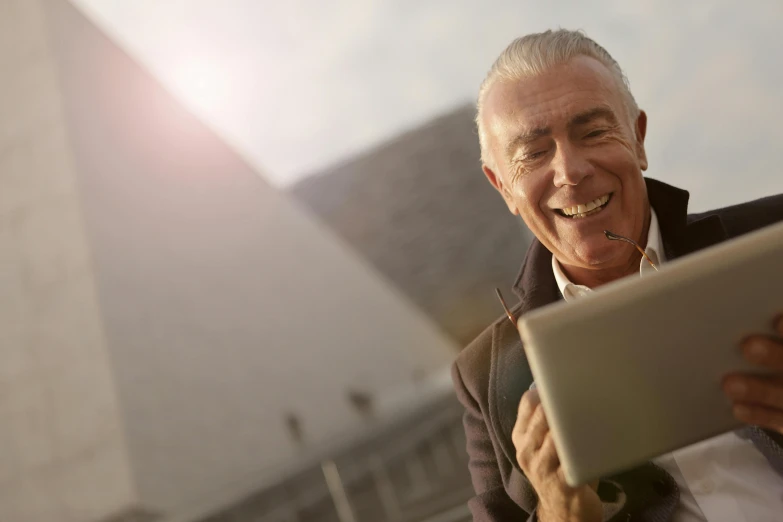 a man smiling while using a tablet computer, a photo, pexels contest winner, pyramid in background, dark grey haired man, superior detail, waist - up