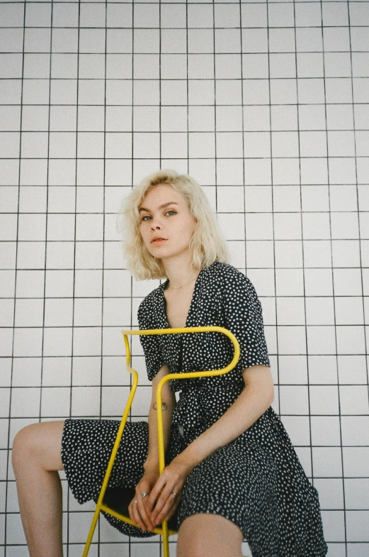 a woman sitting on top of a yellow chair, an album cover, inspired by Elsa Bleda, pexels, pale hair, polka dot, standing, gif