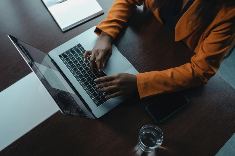 a woman sitting at a table using a laptop computer, trending on pexels, dark grey and orange colours, bottom angle, detailed professional, technical