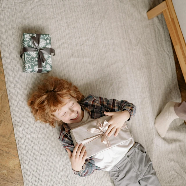 a little boy laying on top of a bed next to a teddy bear, pexels contest winner, holding gift, ( redhead, bird view, on a checkered floor