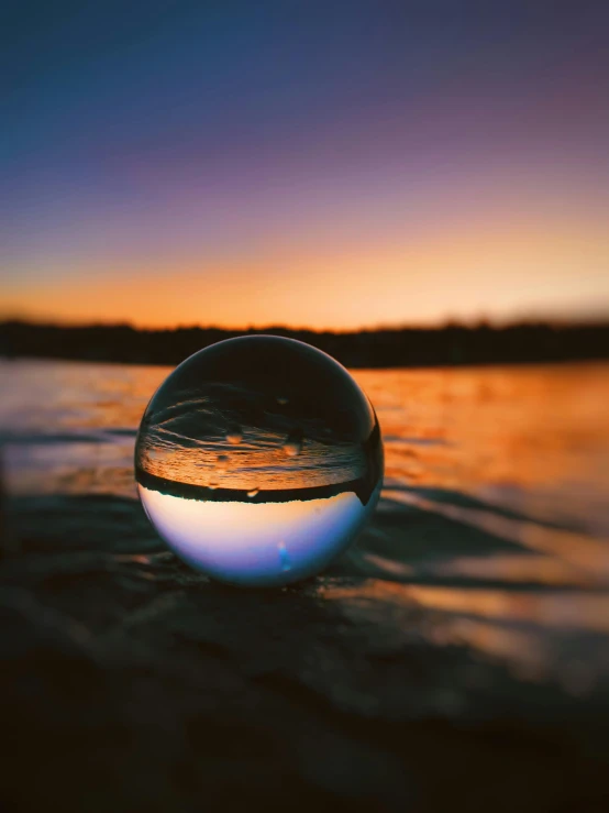 a glass ball sitting on top of a beach, in the middle of a lake