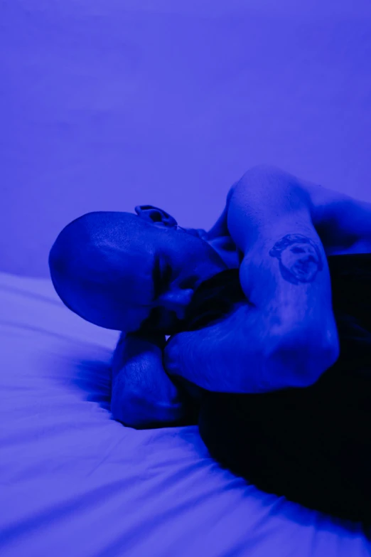 a close up of a person laying on a bed, antipodeans, blue and purle lighting, muscular bald man, contemplation, devastated