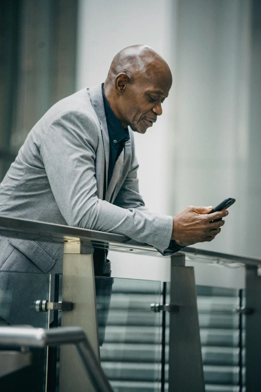 a man in a suit looking at his cell phone, multiple stories, going gray, bald man, black man