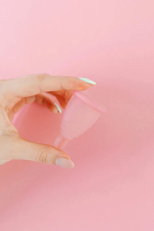 a woman's hand holding a plastic cup against a pink background, plasticien, speculum, how-to, 14mm, bottom - view