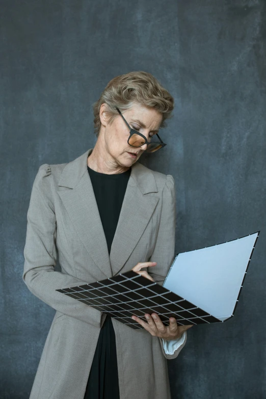 a woman standing in front of a blackboard holding a laptop, an album cover, by Carey Morris, trending on unsplash, older woman, in suit with black glasses, architect studio, inspect in inventory image