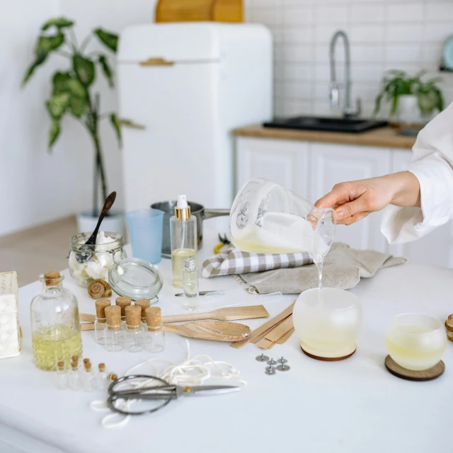 a woman in a white shirt is pouring something into a glass, trending on pexels, process art, ingredients on the table, in a white boho style studio, various items, skincare