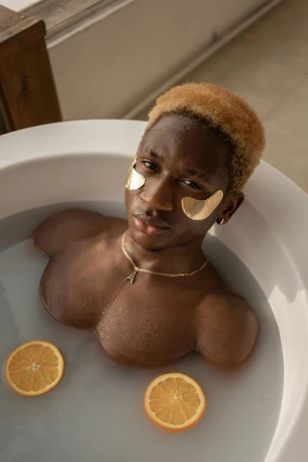a close up of a person in a bath tub with orange slices, inspired by Candido Bido, trending on pexels, afrofuturism, blonde boy with yellow eyes, he is a long boi ”, black skin, cai xukun
