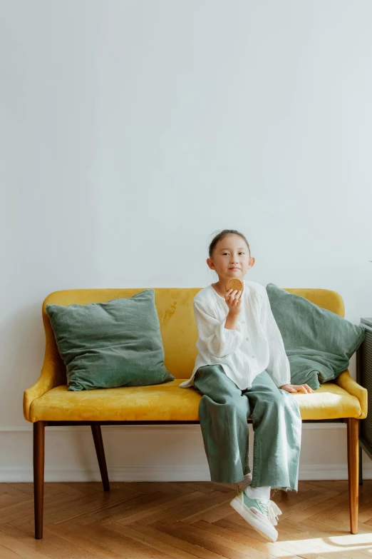 a woman sitting on top of a yellow couch, by Kim Tschang Yeul, pexels contest winner, kid, on a white table, widescreen, green corduroy pants