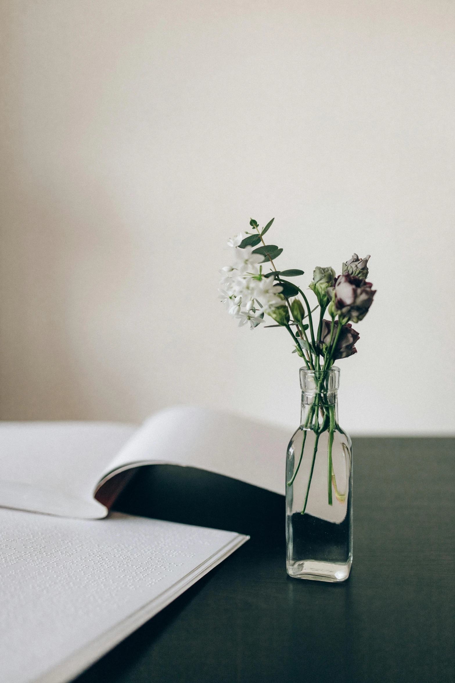 a book sitting on top of a table next to a vase filled with flowers, unsplash, minimalism, papers on table, clear photo, ignant, uncluttered