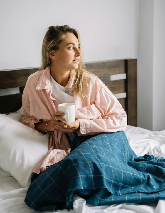 a woman sitting on a bed holding a cup of coffee, by Grace Polit, happening, sydney sweeney, sick with a cold, profile image, pondering