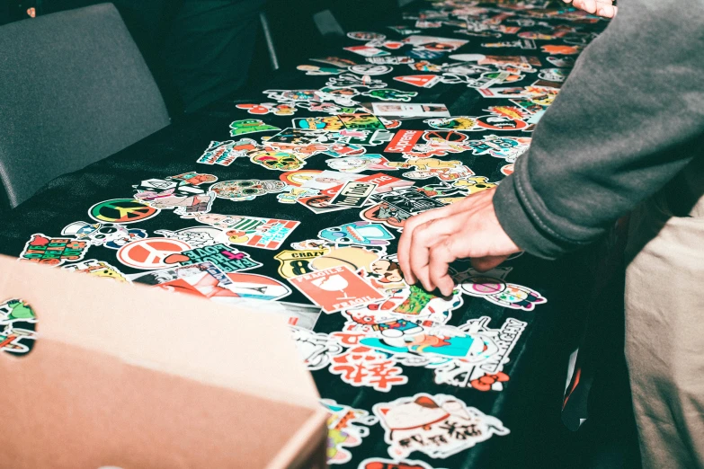 a table with a bunch of stickers on it, a cartoon, trending on unsplash, process art, outlive streetwear collection, back of hand on the table, big crowd, 9 9 designs