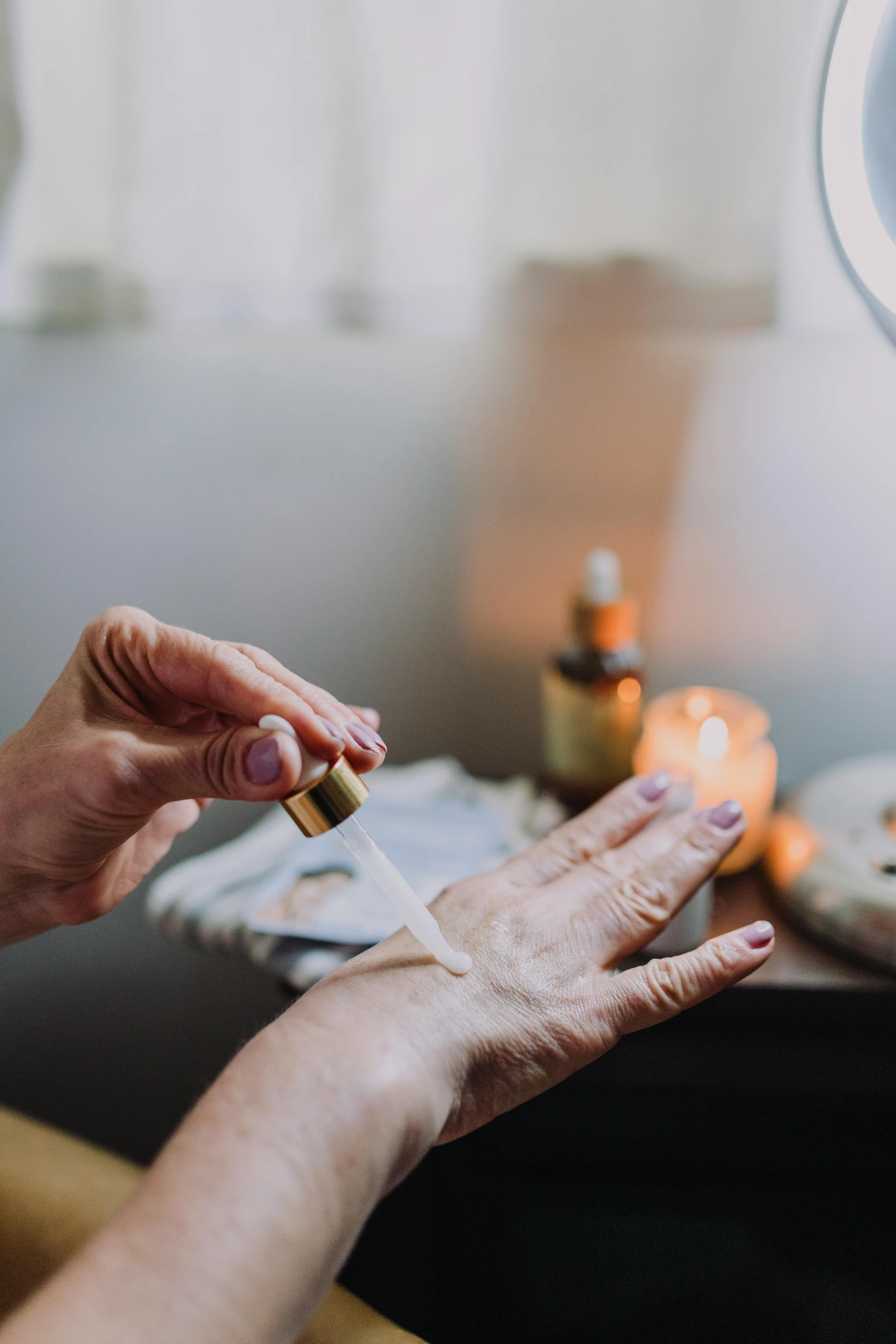 a woman applying her nails in front of a mirror, trending on pexels, casting a spell on a potion, natural candle lighting, white robe with gold accents, paul barson