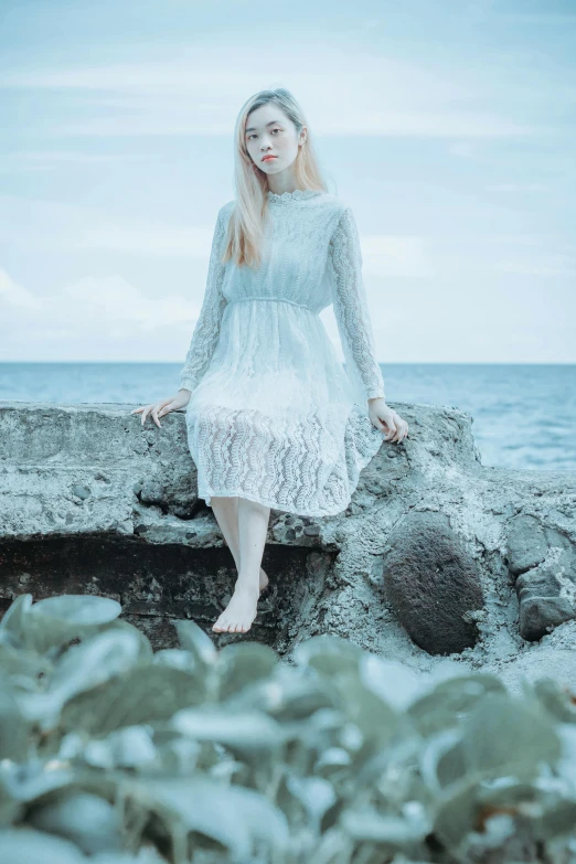 a woman sitting on a rock near the ocean, inspired by Elsa Bleda, romanticism, albino white pale skin, model エリサヘス s from acquamodels, lace dress, dull pastel colors