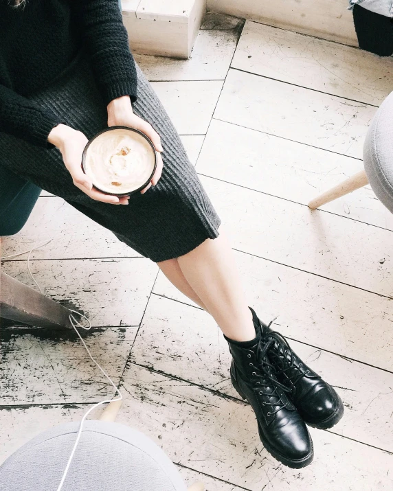 a woman sitting on a chair holding a cup of coffee, by Lucia Peka, trending on unsplash, wearing black boots, instagram picture, outfit: cop, small hipster coffee shop