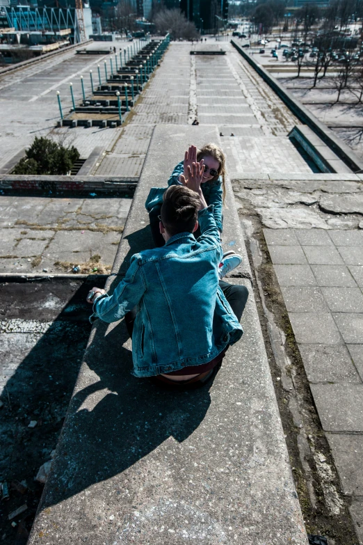 a couple of people sitting on the side of a road, an album cover, inspired by Elsa Bleda, pexels contest winner, happening, inside berghain, blue jacket, sky - high view, aggressive pose