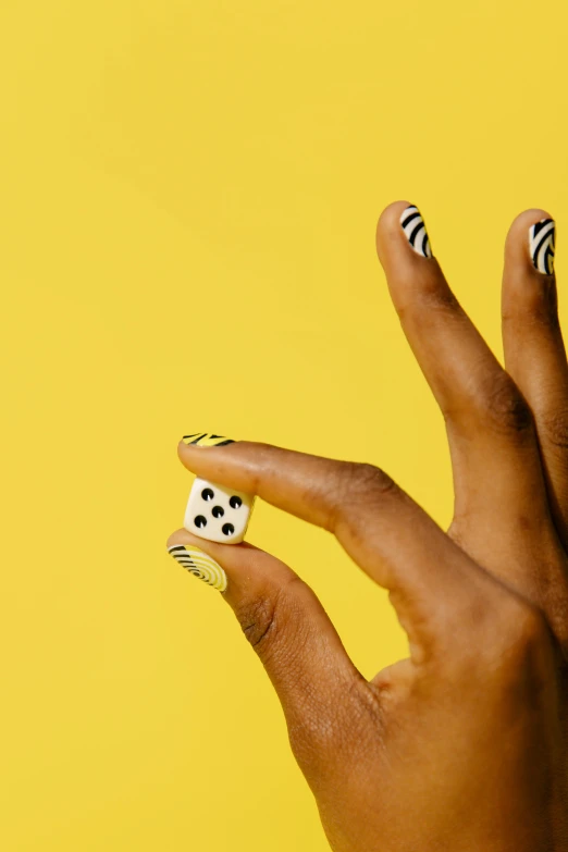 a woman's hand holding a dice on a yellow background, inspired by Yayou Kusama, op art, zebra stripes, maria borges, long nails, medium-shot