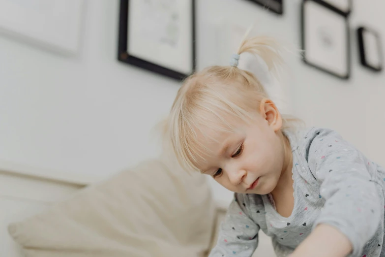 a little girl that is playing with a toy, sitting on a couch, blonde hair with a pony tail, colour corrected, thumbnail