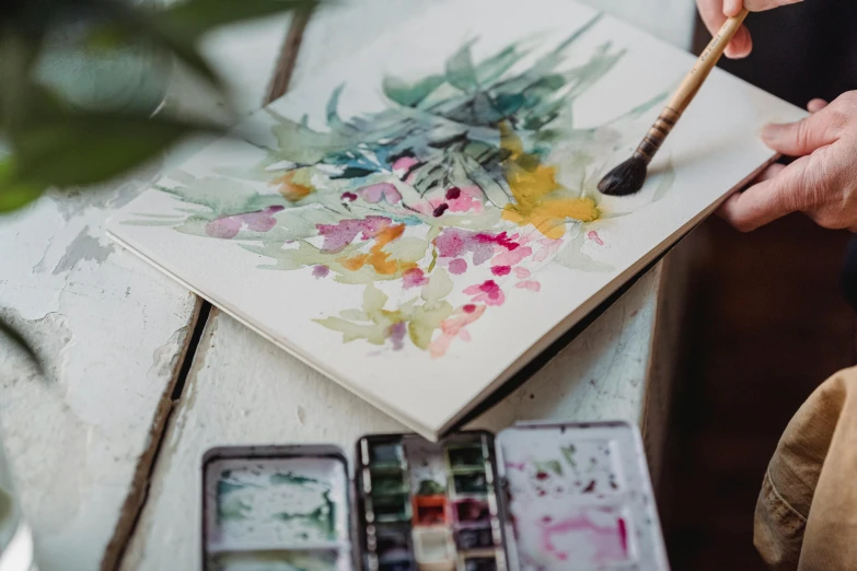 a person painting with a brush on a table, a watercolor painting, trending on pexels, botanicals, fan favorite, art set, well drawn