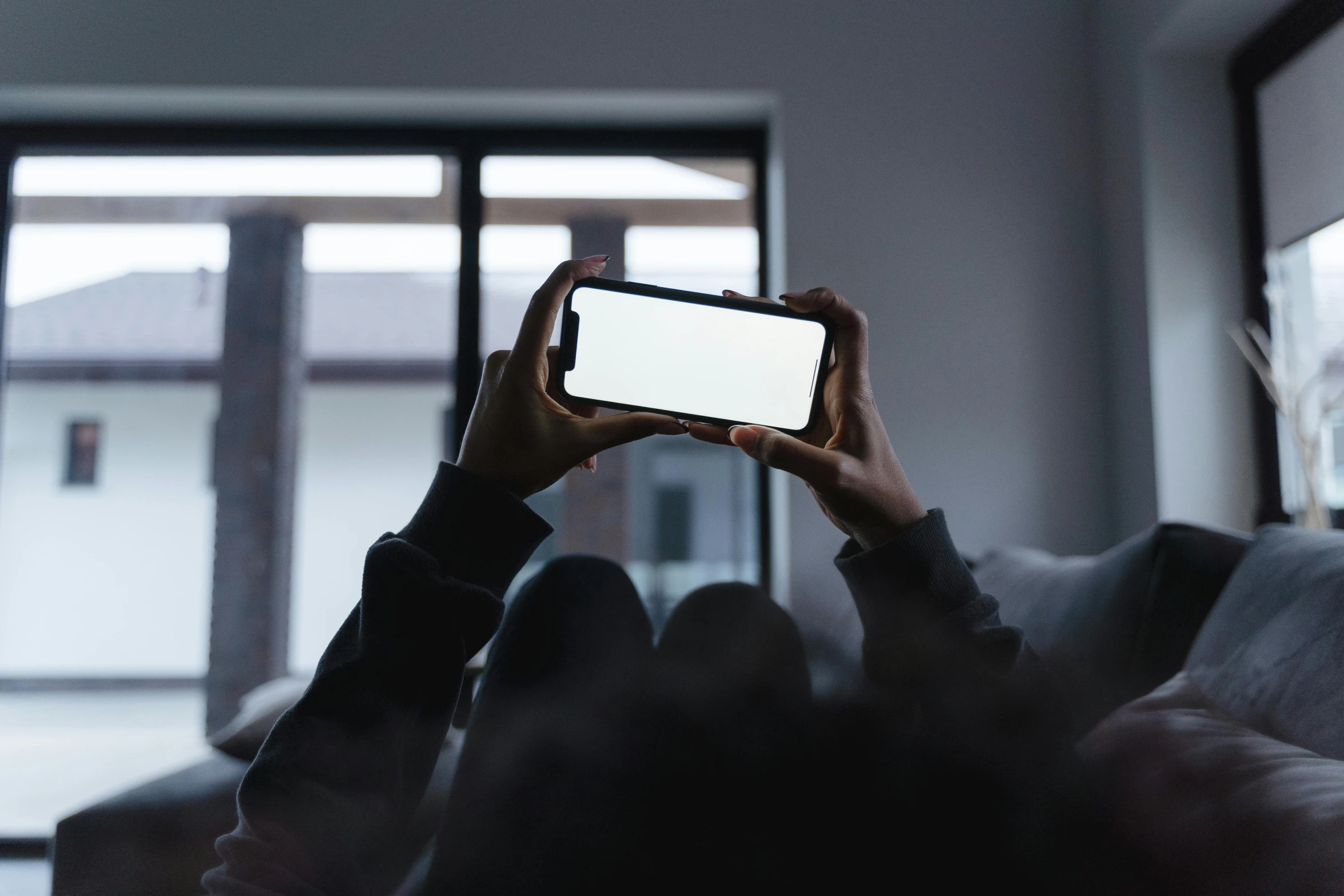 a person sitting on a couch holding up a cell phone, a picture, inspired by Elsa Bleda, unsplash contest winner, group of people in a dark room, on a gray background, natural lighting. 8 k, viewed from behind