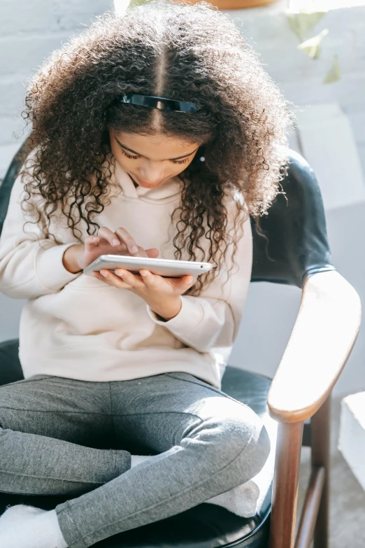 a young girl sitting on a chair using a cell phone, a cartoon, trending on pexels, from reading to playing games, future activist, afro tech, loosely cropped